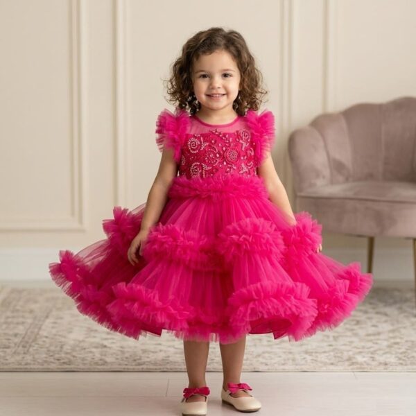 Little girl with curly hair wearing a stunning hot pink layered ruffle tulle party dress with intricate embroidered bodice.
