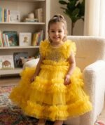 Little girl wearing a bright yellow layered ruffle net party gown with golden floral embroidery.