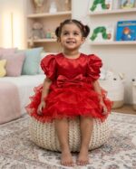 Toddler girl wearing a vibrant red silk-finish puff sleeve dress with a layered ruffle skirt and waist bow