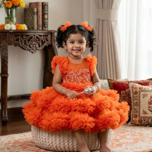 Little girl wearing a bright orange layered ruffle party dress with intricate pearl and floral embroidery on the bodice.