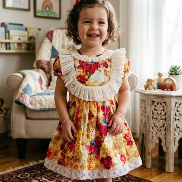 Little girl smiling in a vibrant floral print yellow and red dress with white lace ruffle details.